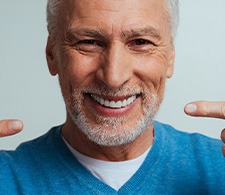 Man in blue shirt pointing to his smile with both hands