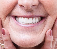 Nose-to-neck view of older woman smiling with hands on cheeks