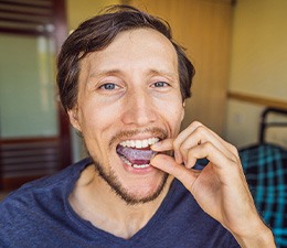 a man putting a nightguard in his mouth while sitting on a bed