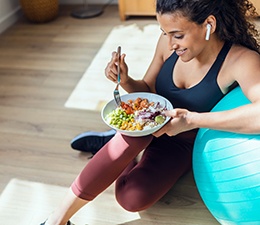 Woman in workout gear leaning on ball eating salad