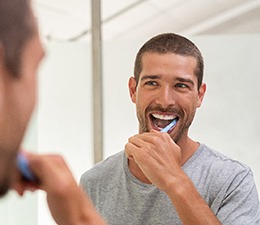 Man smiling while brushing his teeth in bathroom