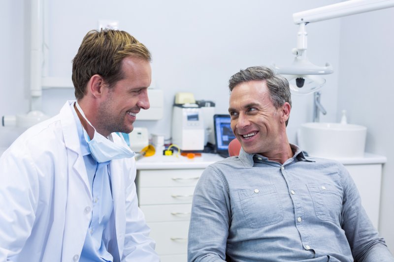 a dentist smiles as he listens to a male patient during an appointment