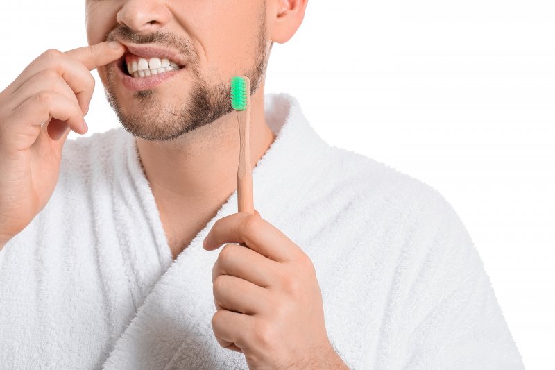 man holding toothbrush pointing to gums