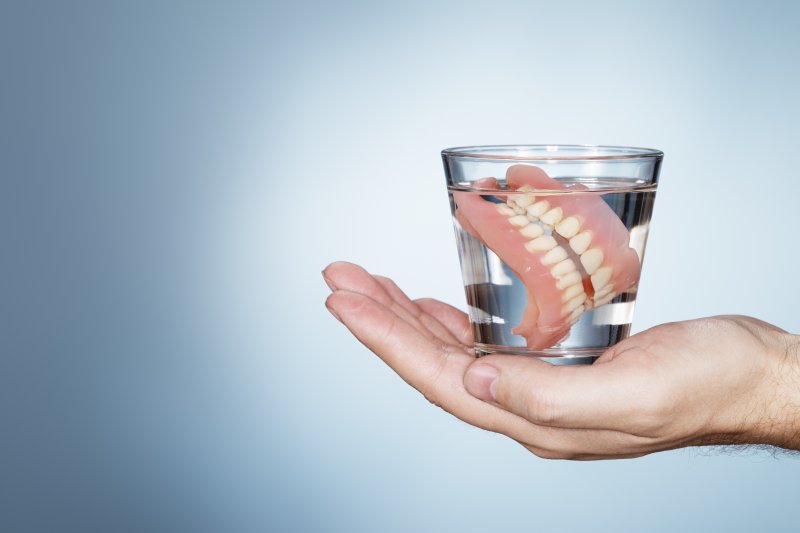 A hand holding a glass that contains dentures in a solution