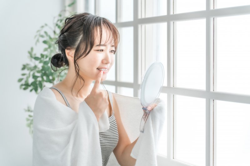 a woman checking her gums and teeth with a mirror