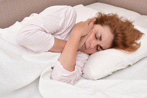 Red-haired woman lying in bed with jaw pain